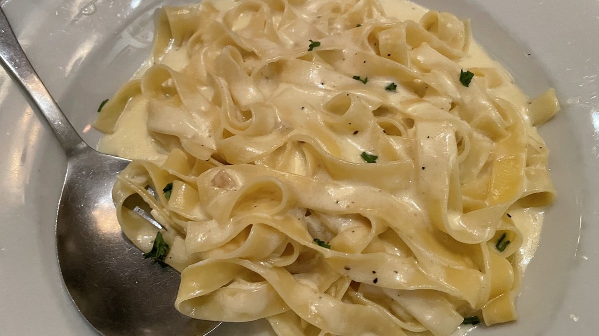 Maydanoz ve karabiberle servis edilmiş parlak soslu fettuccine Alfredo, beyaz tabakta