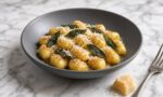 Gri, sade bir tabakta çıtır adaçayı yapraklı tereyağı soslu patates gnocchi, üzerinde rendelenmiş Parmigiano