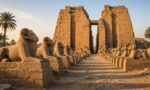 Karnak Tapınağı’nın girişinde koç başlı sfenks sırası ve arkasında yükselen büyük taş pilon, sabah ışığında temsili görsel