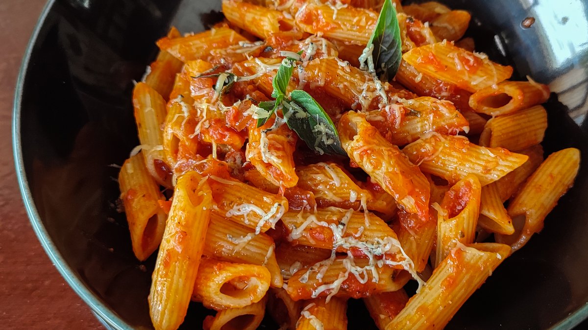 Rendelenmiş peynir ve fesleğenle servis edilmiş penne all'arrabbiata, siyah kasede