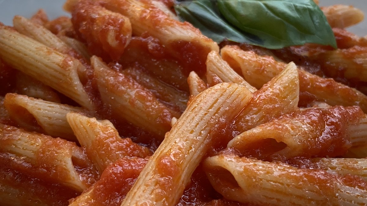 Penne all'arrabbiata yakın plan: domates sosuyla kaplanmış penne rigate ve fesleğen